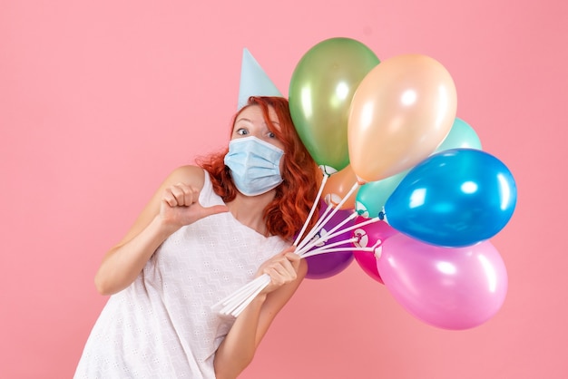 Vue De Face De La Jeune Femme Tenant Des Ballons Colorés En Masque Stérile Sur Le Mur Rose