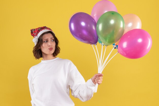 Vue de face de la jeune femme tenant des ballons colorés sur mur jaune