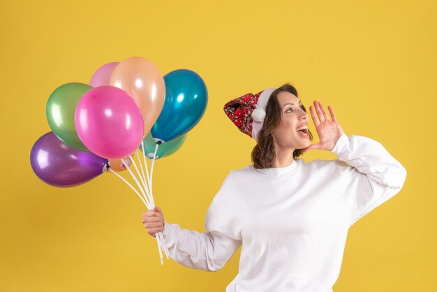 Vue de face de la jeune femme tenant des ballons colorés sur mur jaune