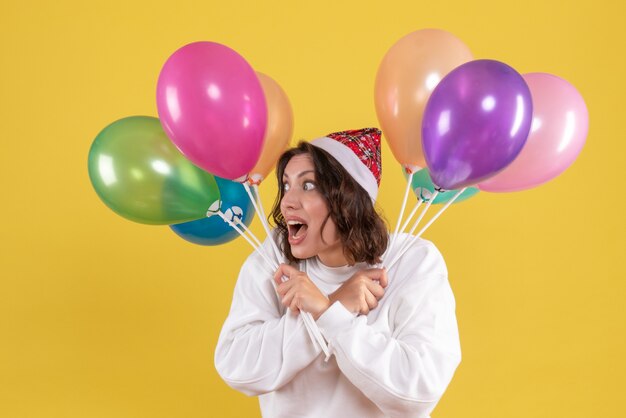 Vue de face de la jeune femme tenant des ballons colorés sur mur jaune