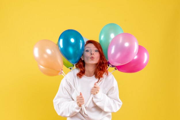 Vue de face de la jeune femme tenant des ballons colorés sur mur jaune