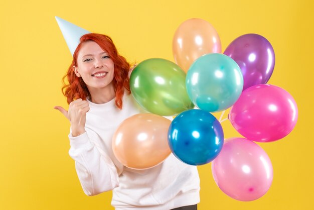 Vue de face de la jeune femme tenant des ballons colorés sur mur jaune