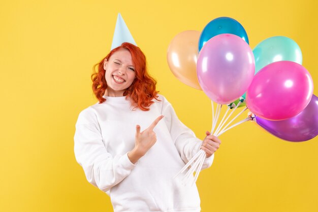 Vue de face de la jeune femme tenant des ballons colorés sur mur jaune