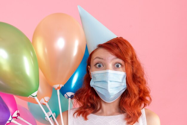 Vue de face de la jeune femme tenant des ballons colorés sur le mur rose