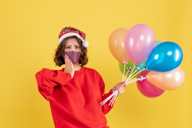 Vue de face jeune femme tenant des ballons sur jaune