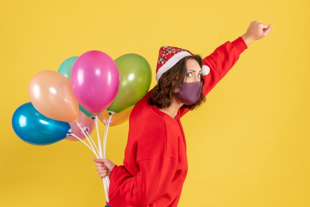 Vue de face jeune femme tenant des ballons en masque sur jaune