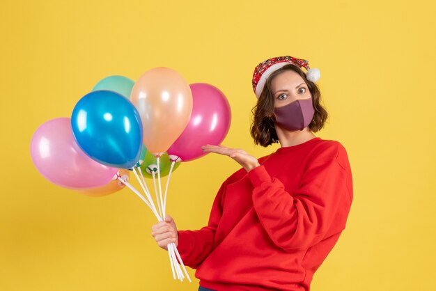 Vue de face jeune femme tenant des ballons en masque sur jaune