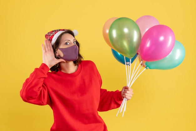 Photo gratuite vue de face jeune femme tenant des ballons en masque stérile sur jaune