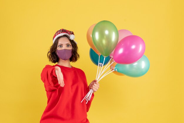 Vue de face jeune femme tenant des ballons en masque stérile sur jaune