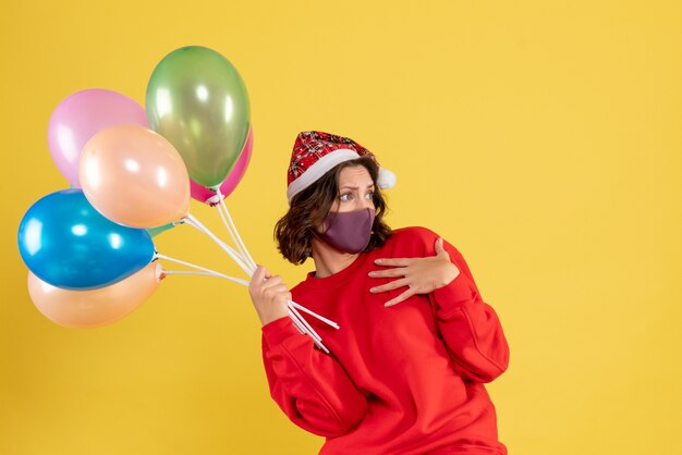 Vue de face jeune femme tenant des ballons en masque stérile sur jaune