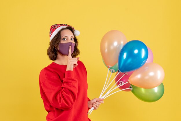 Vue de face jeune femme tenant des ballons en masque stérile sur jaune