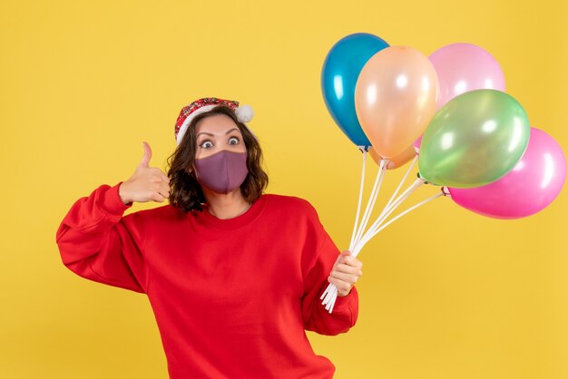 Vue de face jeune femme tenant des ballons en masque stérile sur jaune