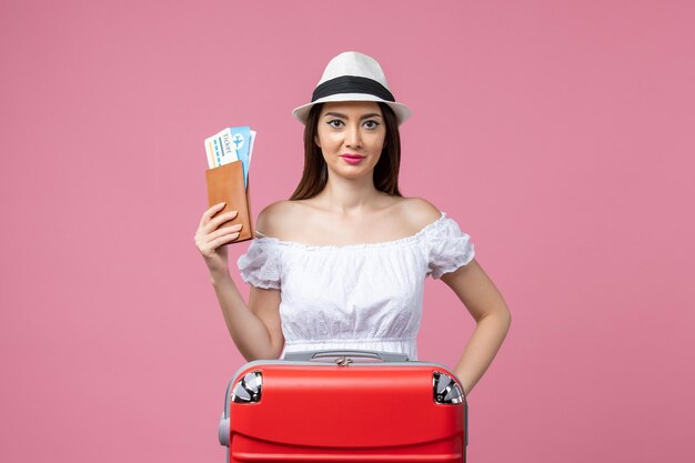 Vue de face jeune femme tenant des billets d'avion pour des vacances sur le mur rose voyage d'été émotion voyage en avion