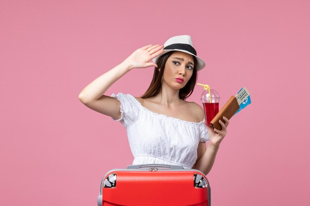 Vue de face jeune femme tenant des billets avec du jus en vacances sur un mur rose clair femme voyage d'été voyage de repos