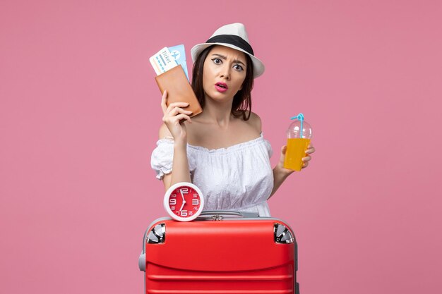 Vue de face jeune femme tenant des billets et du jus en vacances sur le mur rose voyage d'été femme vacances chaleur