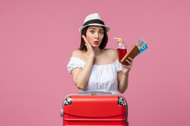 Vue de face jeune femme tenant des billets avec du jus en vacances sur le mur rose voyage femme voyage de repos d'été
