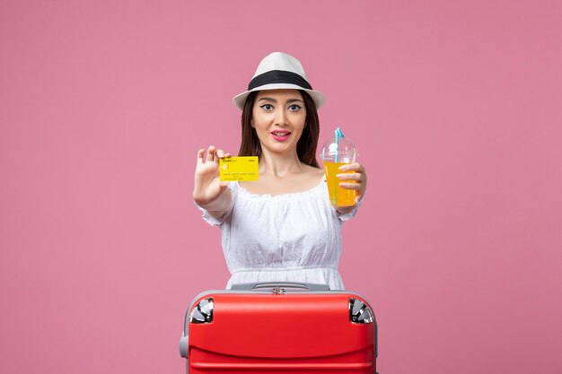 Vue de face jeune femme tenant une boisson et une carte bancaire sur le mur rose voyage vacances été couleur chaleur