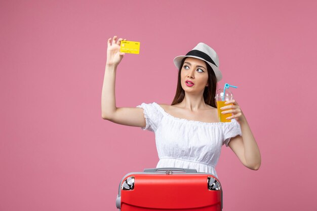 Vue de face jeune femme tenant une boisson et une carte bancaire sur le mur rose voyage vacances été couleur chaleur