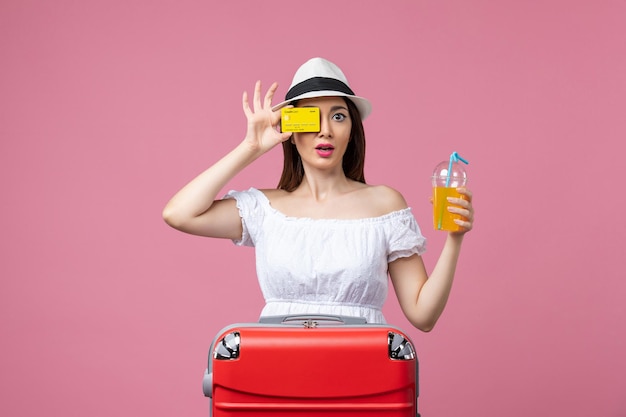 Vue de face jeune femme tenant une boisson et une carte bancaire sur le mur rose voyage vacances été voyage couleurs chaudes