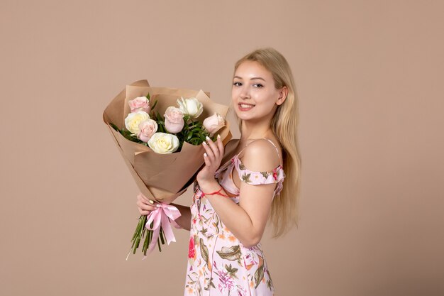Vue de face d'une jeune femme tenant un bouquet de belles roses sur un mur marron