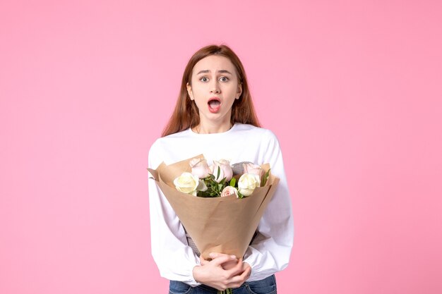 Vue de face jeune femme tenant un bouquet de belles roses sur rose