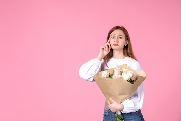 Vue de face jeune femme tenant un bouquet de belles roses sur rose