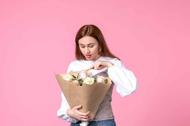 Vue de face jeune femme tenant un bouquet de belles roses sur rose