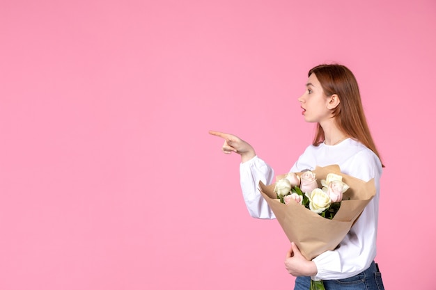 Vue de face jeune femme tenant un bouquet de belles roses sur rose
