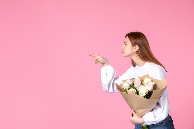 Vue de face jeune femme tenant un bouquet de belles roses sur rose