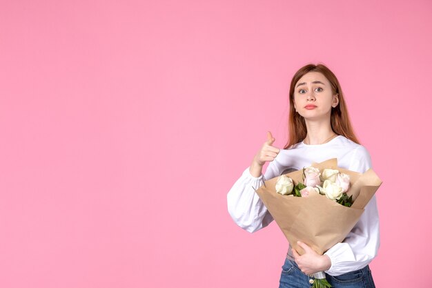 Vue de face jeune femme tenant un bouquet de belles roses sur rose