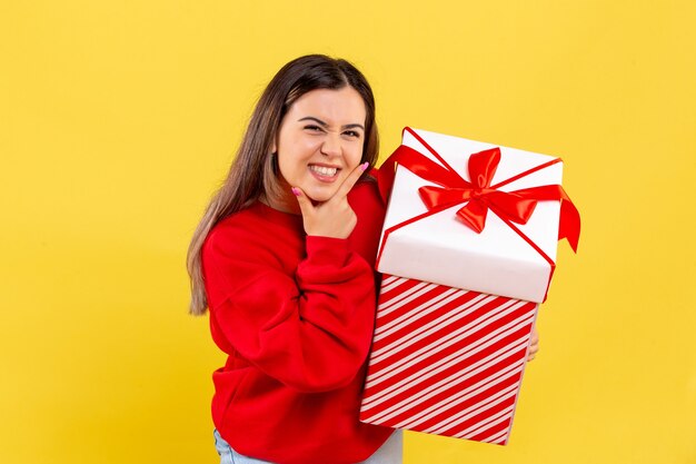 Vue de face de la jeune femme tenant un cadeau de Noël en boîte sur mur jaune