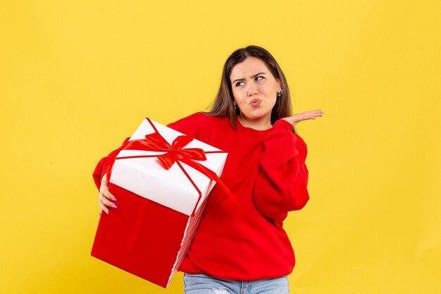 Vue de face jeune femme tenant un cadeau de Noël sur fond jaune