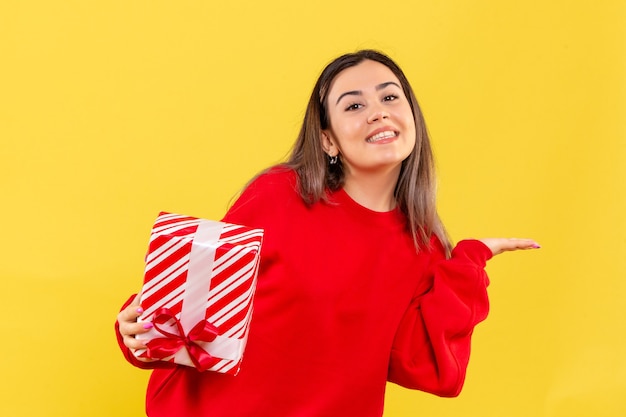 Vue de face de la jeune femme tenant un cadeau de Noël avec sourire sur mur jaune