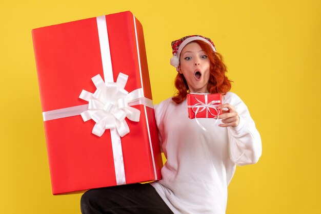 Vue de face de la jeune femme tenant des cadeaux de Noël sur mur jaune