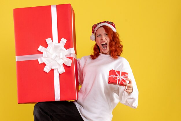 Vue de face de la jeune femme tenant des cadeaux de Noël sur mur jaune