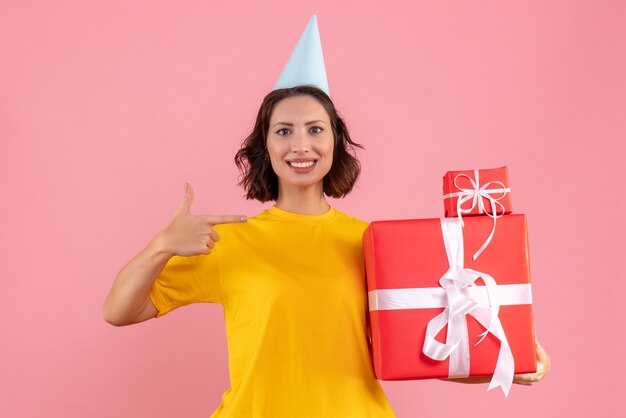 Vue de face de la jeune femme tenant des cadeaux de Noël sur le mur rose