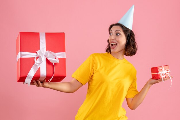 Vue de face de la jeune femme tenant des cadeaux de Noël sur le mur rose