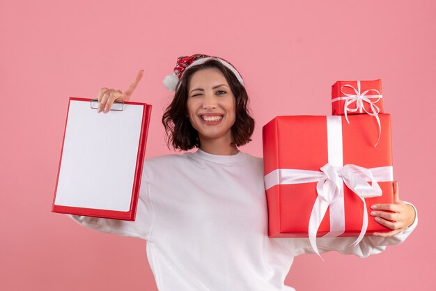 Vue de face de la jeune femme tenant des cadeaux de Noël sur le mur rose