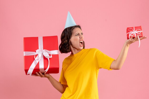 Vue de face de la jeune femme tenant des cadeaux de Noël sur le mur rose