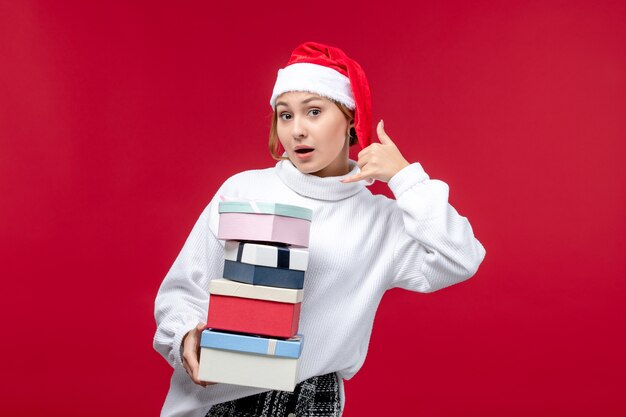 Vue de face jeune femme tenant des cadeaux de nouvel an sur un bureau rouge