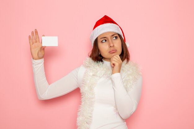 Vue de face jeune femme tenant une carte bancaire blanche sur mur rose vacances de Noël nouvel an mode couleur argent