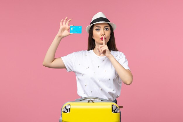 Vue de face jeune femme tenant une carte bancaire bleue sur un bureau rose voyage couleur voyage été