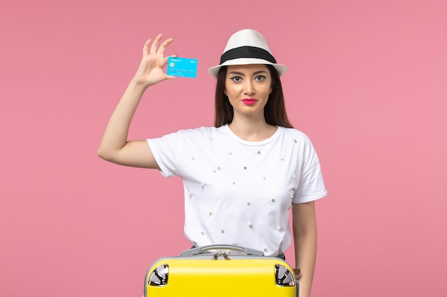 Vue de face jeune femme tenant une carte bancaire bleue sur un mur rose voyage couleur voyage été