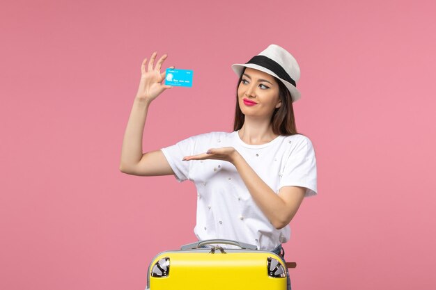 Vue de face jeune femme tenant une carte bancaire bleue sur le mur rose voyage voyage été