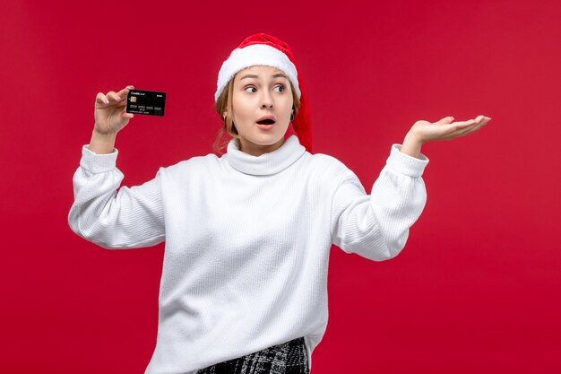 Vue de face jeune femme tenant une carte bancaire sur un bureau rouge