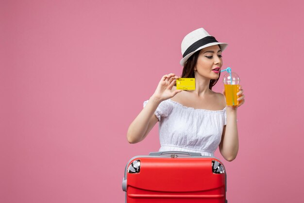 Vue de face jeune femme tenant une carte bancaire et un cocktail sur le mur rose été voyage voyage couleur chaleur vacances