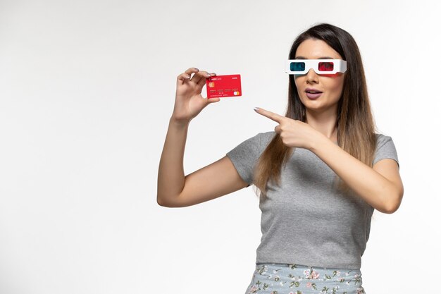 Vue de face jeune femme tenant une carte bancaire dans des lunettes de soleil sur une surface blanche claire