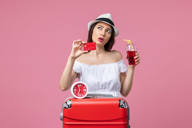 Vue de face jeune femme tenant une carte bancaire et du jus en vacances sur le mur rose voyage voyage femme d'été