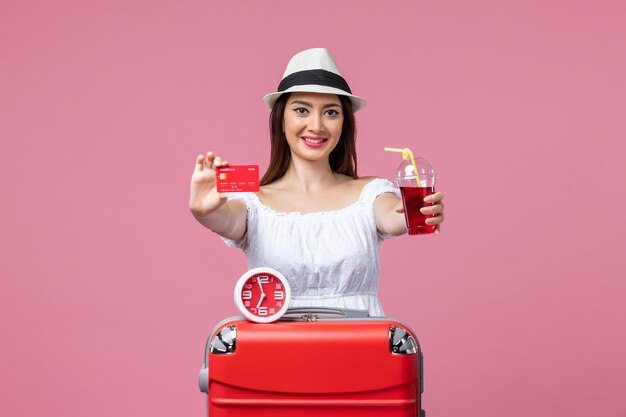 Vue de face jeune femme tenant une carte bancaire et du jus en vacances sur un mur rose voyage voyage vacances d'été femme