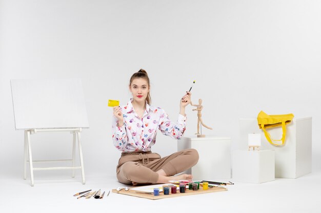 Vue de face jeune femme tenant une carte bancaire jaune sur fond blanc